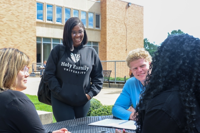 Four Holy Family University students sitting at an outdoor table on campus having a conversation