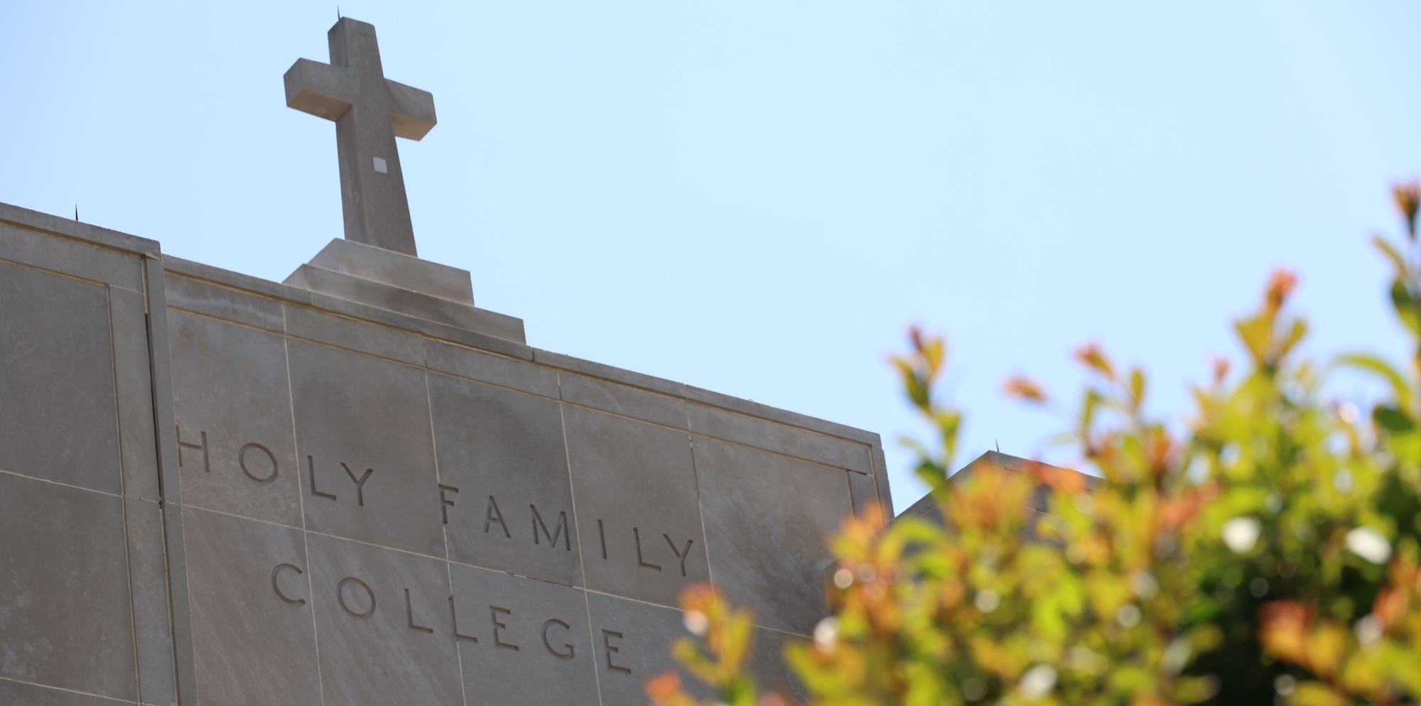 The facade of a campus building with "Holy Family College" engraved in it