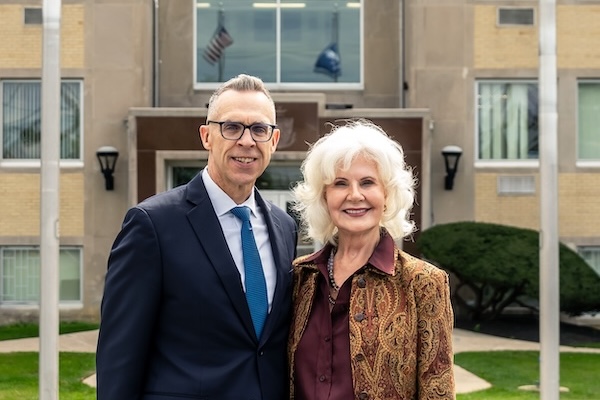 Linda Thatcher Raichle &amp; Jim Bennett standing in front of Holy Family Hall