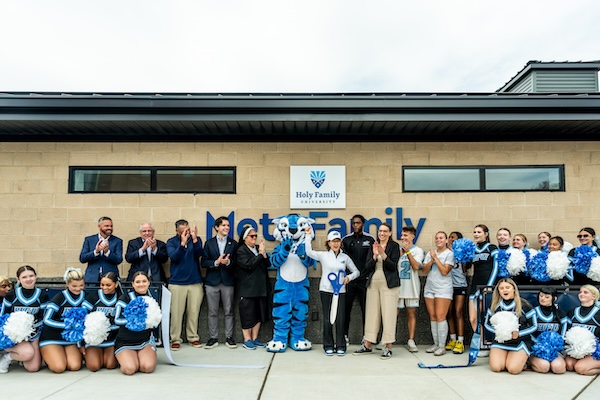 A crowd of Holy Family representatives and athletes celebrate the dedication of the new Metz Fieldhouse with the university president