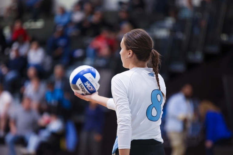 A women's volleyball player prepares to serve in front of a large crowd