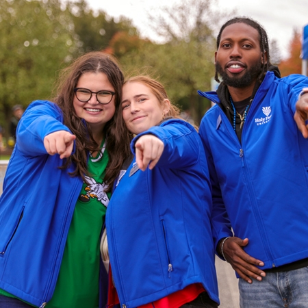 Three HFU alumni pose at a campus event all wearing the same Holy Family University jacket