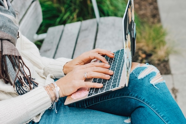A woman sitting on an outdoor bench working on a laptop