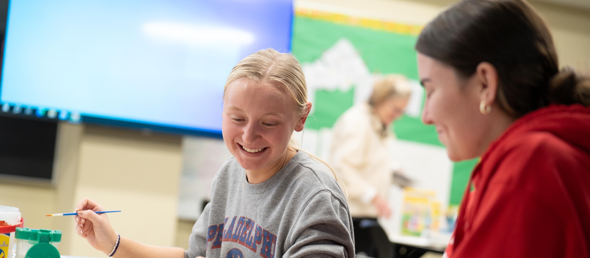 Two students in a classroom smiling and working together on a project