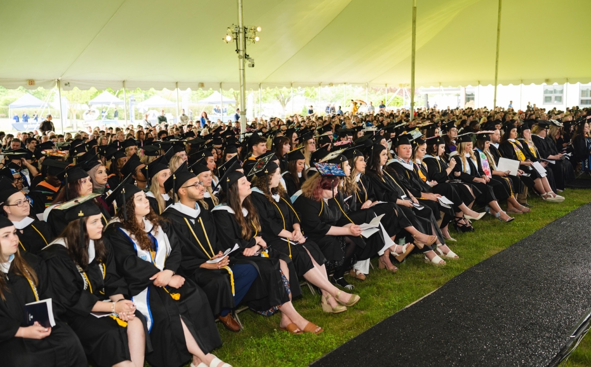 Large crowd of HFU students in caps and gowns sitting under a tent during 2024's Commencement