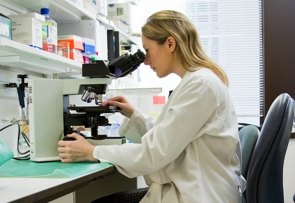 A scientist in a lab sitting in a chair while looking into a microscope