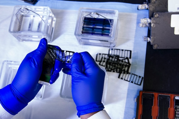 A scientist's hands wearing rubber gloves working with a sample over a lab table
