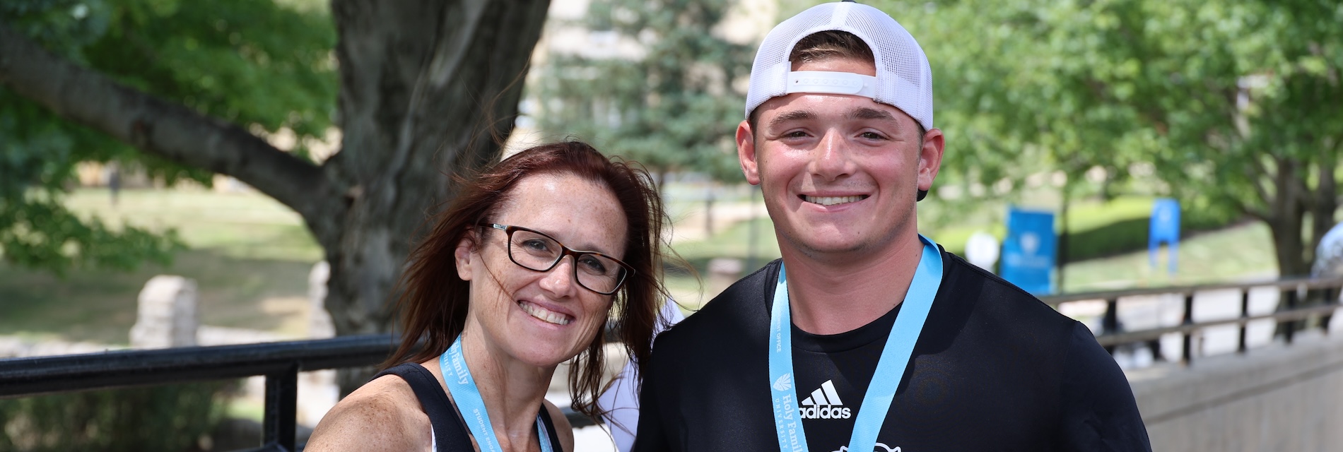 An HFU student and his mother smile while wearing Holy Family shirts
