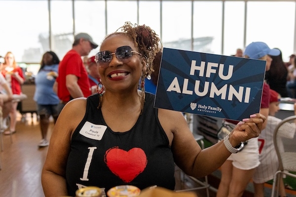 A Holy Family alum at the Phillies takeover holding an "HFU Alumni" sign