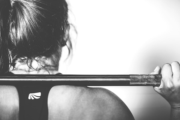 Woman in exercise gear with a weight bar resting on her shoulders