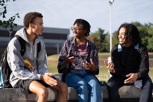Three students sitting outside on campus talking and smiling