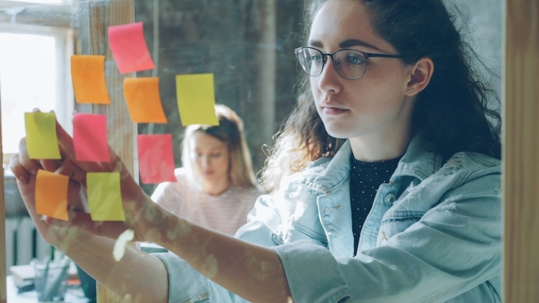 Business school student putting up post-its with colleagues, working on a project